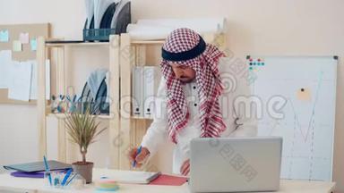 现代中东人，穿着民族服装，在办公桌前的办公室工作。 头上戴着古特拉的商人